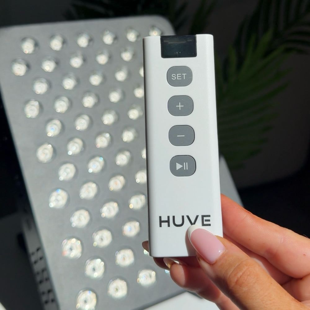 HUVE LUMA Glow remote in hand with Black Premium Red Light Therapy Panel with 9 therapeutic wavelengths in the background