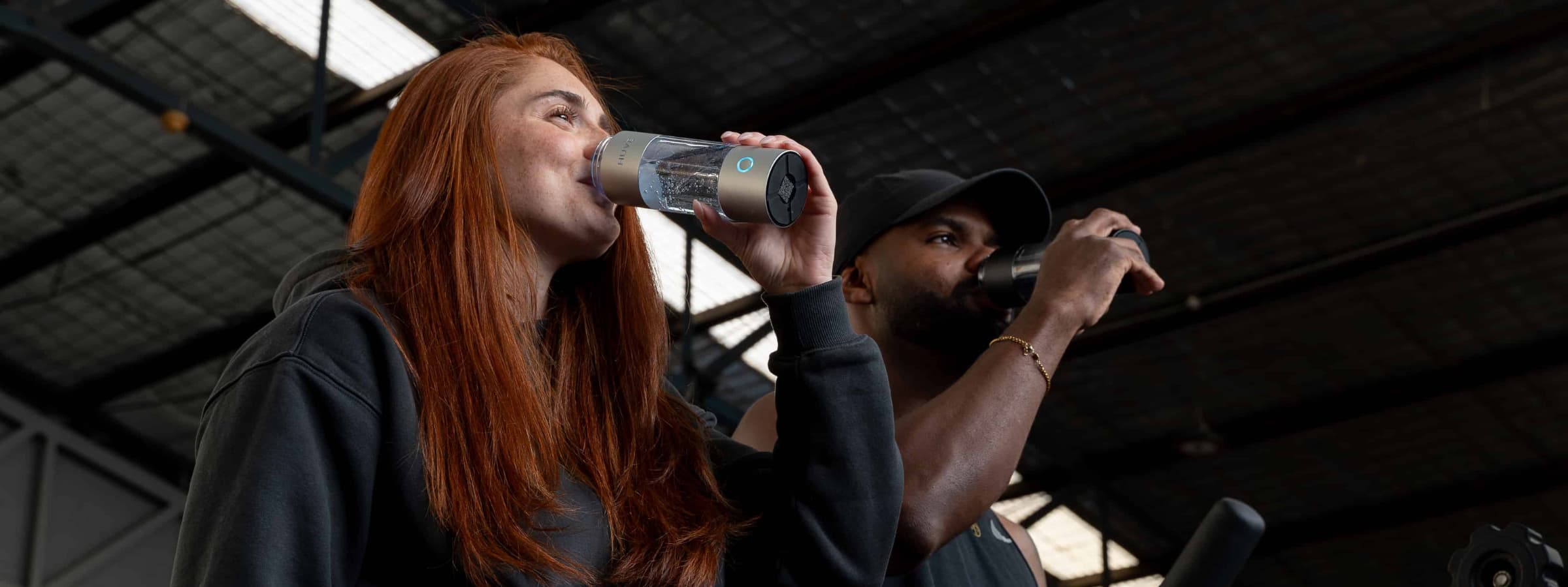 Two people drinking from HUVE hydrogen water bottles in a gym