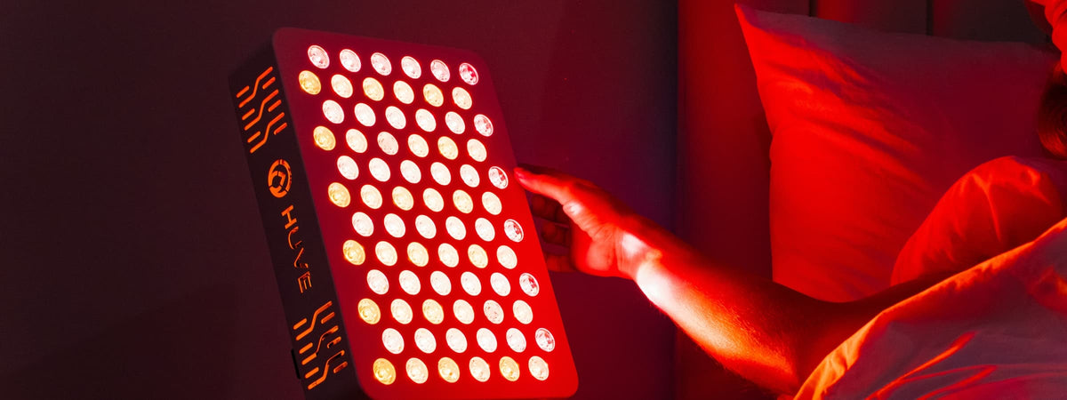Woman adjusting a HUVE Luma red light therapy panel in bed
